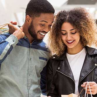 a man and a woman standing together looking inside bags of items recently purchased at the mall